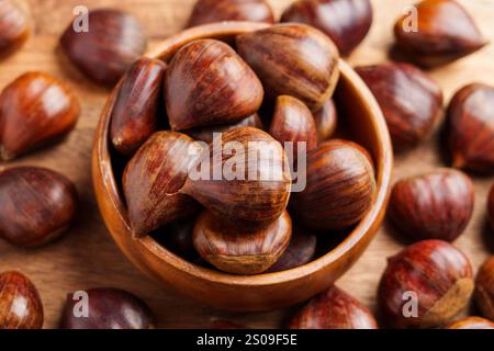 Wooden bowl with fresh harvested chestnuts and scattered organic nuts on rustic table. Close up. Top view Stock Photo
