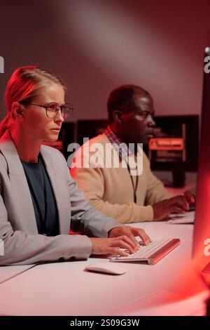 Young IT support manager in formalwear looking at computer screen while solving technical problem against male coworker Stock Photo
