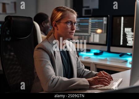 Serious female IT support manager typing on keypad and looking at computer screen against male coworker Stock Photo