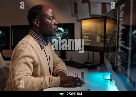 Serious male IT engineer keeping hand on computer mouse and looking at screen while developing new software in office Stock Photo