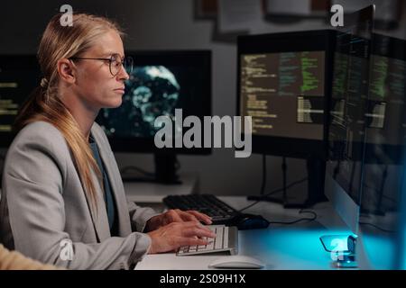 Side view of young serious woman concentrating on solving technical problem or decoding data and typing on computer keypad Stock Photo