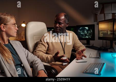 Confident male programmer explaining ways of decoding data to blond female colleague during conversation at meeting Stock Photo
