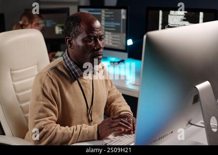 Experienced male IT support manager decoding data while sitting in front of desktop computer monitor and looking at screen Stock Photo