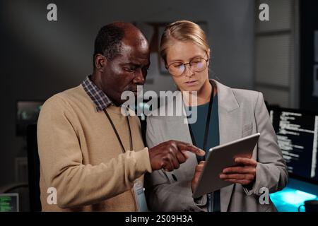 Confident mature African American IT engineer pointing at tablet screen while explaining young colleague online data Stock Photo