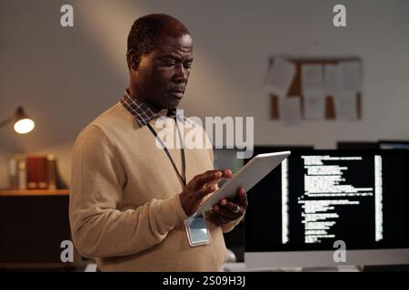 Mature male IT engineer scrolling on tablet screen while decoding online data or testing new software in front of camera Stock Photo