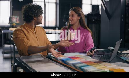 Multiracial couple creative designers work in modern office studio Arabian Indian man Caucasian woman using phone choosing perfect sample of material Stock Photo