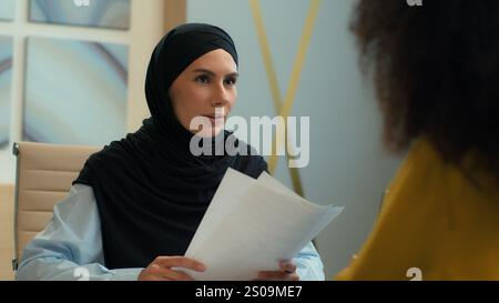 Two business partners women girls Muslim woman businesswoman in hijab real estate agent consult African female client at office meeting discuss Stock Photo