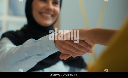 Happy smiling muslim islamic woman in hijab businesswoman recruit client handshake shake arms female business partners colleagues shaking hands deal Stock Photo
