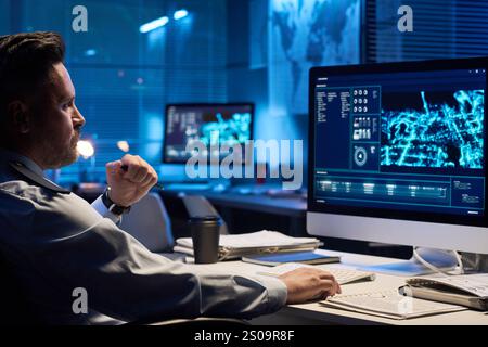 Young serious male operator in uniform looking at graphic data on computer screen while sitting by workplace Stock Photo