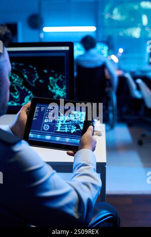 Male officer holding digital tablet with graphic data on screen while sitting by workplace and analyzing military location Stock Photo