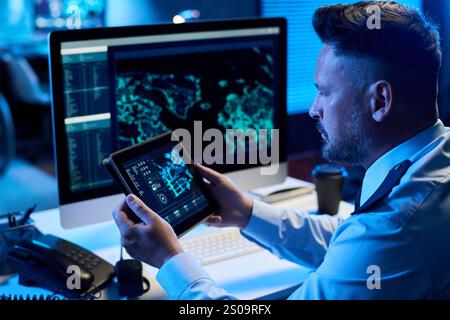 Serious mature man in uniform sitting by workplace in military command center and learning graphic data on tablet screen Stock Photo