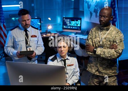 Serious mature woman and her two intercultural male colleagues in uniform looking at desktop computer screen Stock Photo