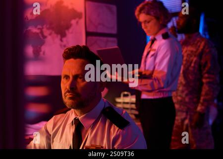 Mature male worker of military command center looking at computer screen while analyzing online data against coworkers Stock Photo