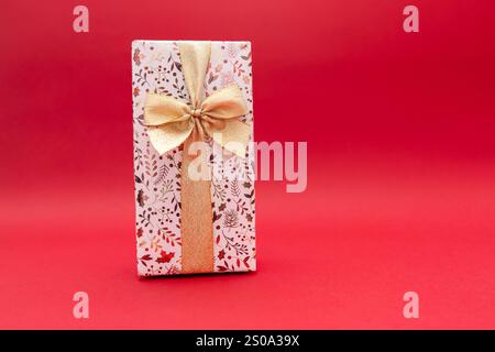 Wrapped gift on bright red background with gold ribbon, birthday gift, Valentine's Day, New Year. Gift is golden and shiny Stock Photo