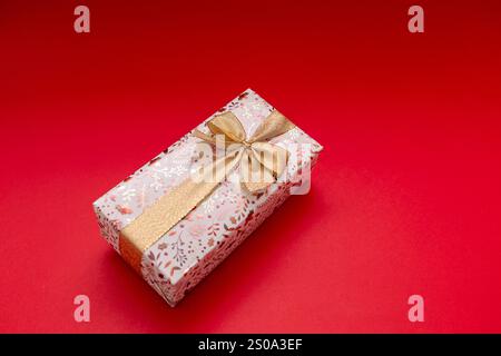 Wrapped gift on bright red background with gold ribbon, birthday gift, Valentine's Day, New Year. Gift is golden and shiny Stock Photo
