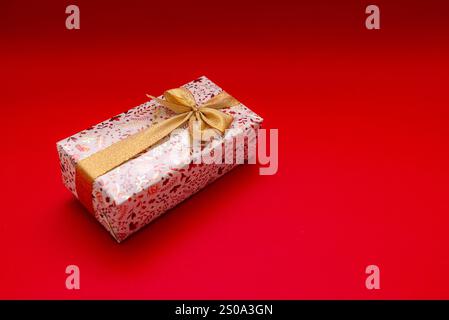 Wrapped gift on bright red background with gold ribbon, birthday gift, Valentine's Day, New Year. Gift is golden and shiny Stock Photo