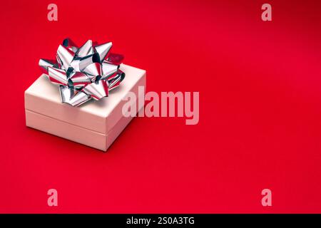 small white gift box with silver ribbon and bow on a bright red background, holiday concept Stock Photo