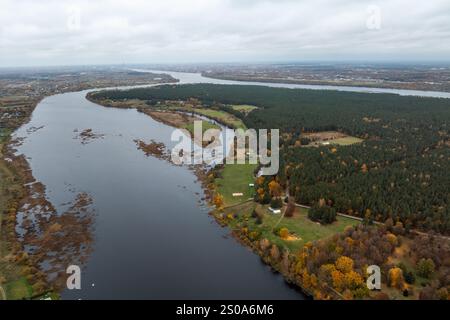 Aerial perspective of a river winding through forests and fields with autumn colors. A cityscape is visible on the horizon under an overcast sky. Stock Photo