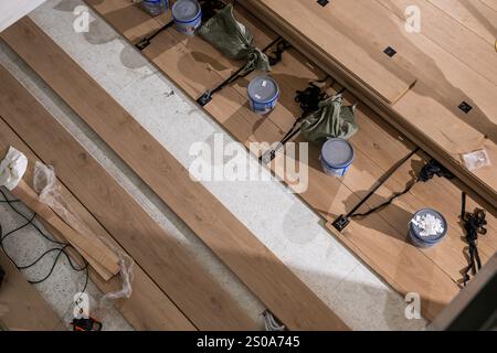 Wooden floorboards are laid on a concrete subfloor with clamps and paint cans used as weights, illustrating the methodical flooring installation proce Stock Photo
