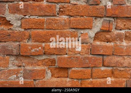 Close-up of an old red brick wall with visible weathering, cracks, and irregular mortar, showcasing a rustic and vintage architectural texture Stock Photo