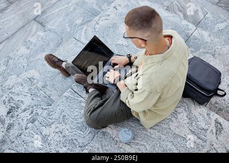Top view of unrecognizable male IT developer code programming on laptop while sitting on concrete steps working outside in city, copy space Stock Photo