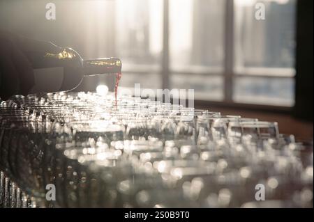 a waiter pouring red wine from bottle to wineglass that set up for dinner reception party in evening time. photo has some flare effect from back light Stock Photo