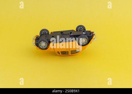 Yellow toy Volkswagen classic Beetle diecast car laying upside down on a yellow background. Stock Photo