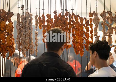 Young men standing in front of kebab meat shop with chicken hanging on sticks in Delhi India Stock Photo