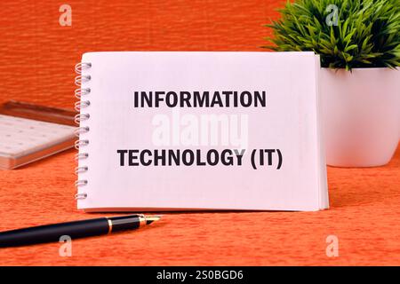 Startup office or people teamwork concept. INFORMATION TECHNOLOGY (IT) written on a clean notebook on an orange background. Stock Photo