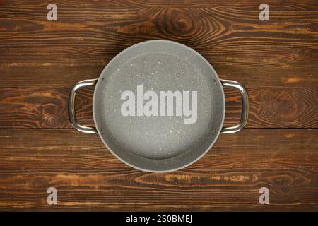 A nonstick cooking pot is placed on a rustic wooden table, showcasing a smooth surface and sturdy handles for various culinary tasks in a warm kitchen Stock Photo