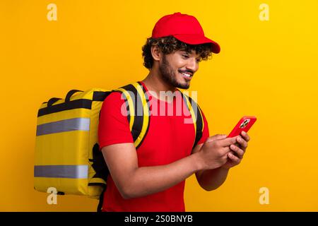 Cheerful courier with yellow backpack using smartphone on a vibrant colored background. Stock Photo
