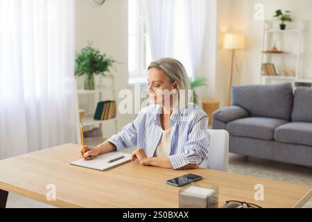 Senior Woman Writing Business Plan in Notepad at Home Stock Photo