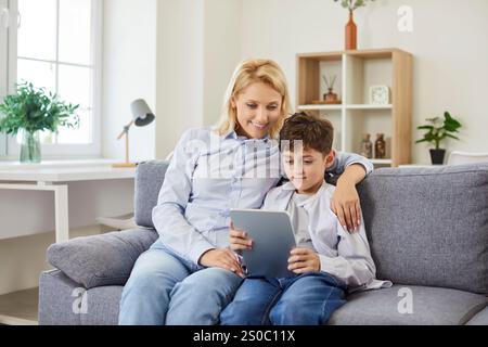 Mother, nanny and child son at home sitting using digital computer tablet applications, choosing Stock Photo