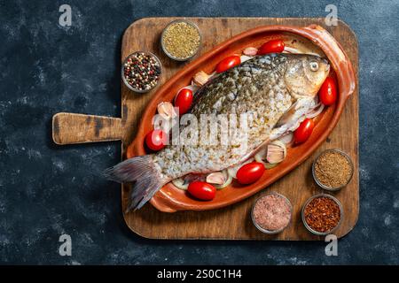 Marinated big fish crucian carp with herbs and spices in clay baking dish on chopping board, close up, top view Stock Photo