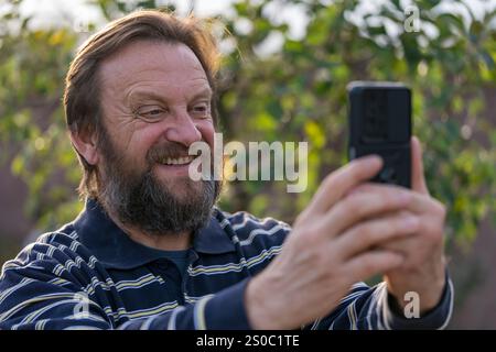 Happy senior adult man rest in nature get message from old friend. Mature man reading good news on phone screen. Elderly male with mobile cell phone Stock Photo
