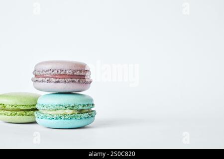 Stack of three colorful French Macarons, cakes with different flavors stacked in a pyramid, mint, apple, currant flavor. macaroons aquamarine, green, purple color on gray background, side view Stock Photo