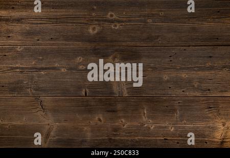 Weathered wooden planks creating a rustic background with dark brown tones, knots, and cracks Stock Photo