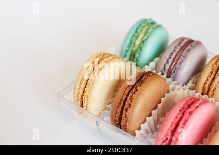 French Macarons with white paperpan in plastic transparent packaging box on gray background, colorful cakes with various flavors. appetizing dessert, macaroons. Copy space for text, top view Stock Photo