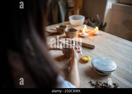Female ceramist molds clay cup with decorative pattern on wood table in workshop. DIY, master class Stock Photo