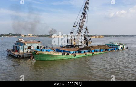 Thuong Phuoc gate, Mekong Delta, Vietnam. December 27,2024: Platforms with crane & clamshell dredge the waterway & load cargo ships/barges. Sand & gravel extraction (mining or dredging) used for concrete in construction industry raises warnings about the environmental impact of overexploitation of river bed sediments (biodiversity & ecosystem), but also about the lives of people living on riverbanks. Legal or illegal sand exploitation leads to massive erosion of banks, resulting in the loss of agricultural land but also the collapse of buildings & houses. Credit: KEVIN IZORCE/Alamy Live News Stock Photo