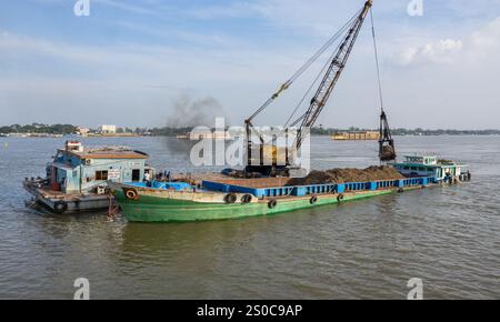 Thuong Phuoc gate, Mekong Delta, Vietnam. December 27,2024: Platforms with crane & clamshell dredge the waterway & load cargo ships/barges. Sand & gravel extraction (mining or dredging) used for concrete in construction industry raises warnings about the environmental impact of overexploitation of river bed sediments (biodiversity & ecosystem), but also about the lives of people living on riverbanks. Legal or illegal sand exploitation leads to massive erosion of banks, resulting in the loss of agricultural land but also the collapse of buildings & houses. Credit: KEVIN IZORCE/Alamy Live News Stock Photo