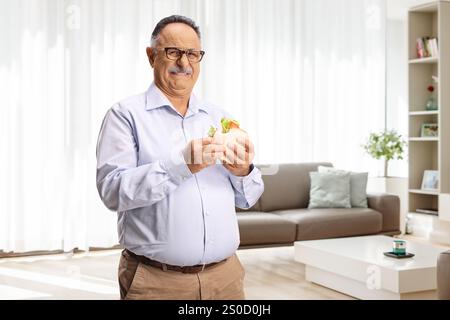 Mature man holding a sandwich and making a grimace at home Stock Photo