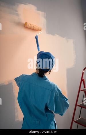 Professional painter in overalls paints metal wall of building with ...