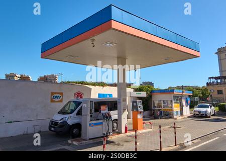 Civitavecchia. Italia - December 17, 2024: White van refueling at urban gas station with multiple pumps and red and white poles. Signs and fire exting Stock Photo