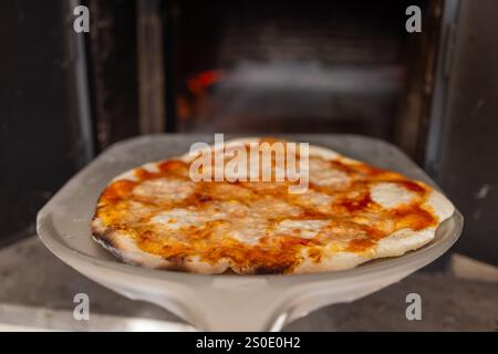 A freshly baked pizza resting on a pizza peel, ready to be served from a rustic wood-fired oven. Stock Photo