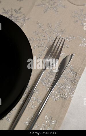 Christmas and New Year festive table setting for one person, closeup black plate with fork and knife on snowflake pattern tablecloth Stock Photo