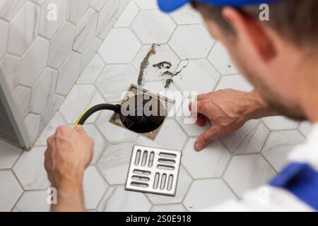 plumber unclogging blocked shower drain with hydro jetting at home bathroom. sewer cleaning service Stock Photo