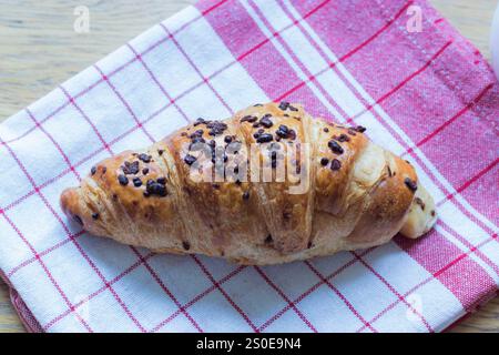 Chocolate croissant with chocolate chip sprinkles on white and red tea towel Stock Photo
