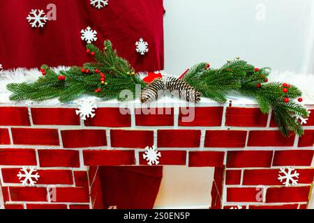 A cozy red brick fireplace is adorned with evergreen branches, pine cones, and small red berries, creating a festive atmosphere perfect for the holida Stock Photo