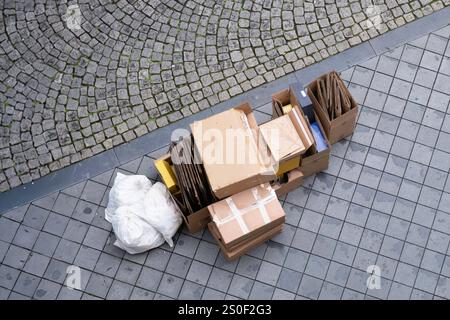 Garbage in white plastic bag and empty cardboard boxes, partially folded, waiting on the sidewalk for the garbage truck Stock Photo